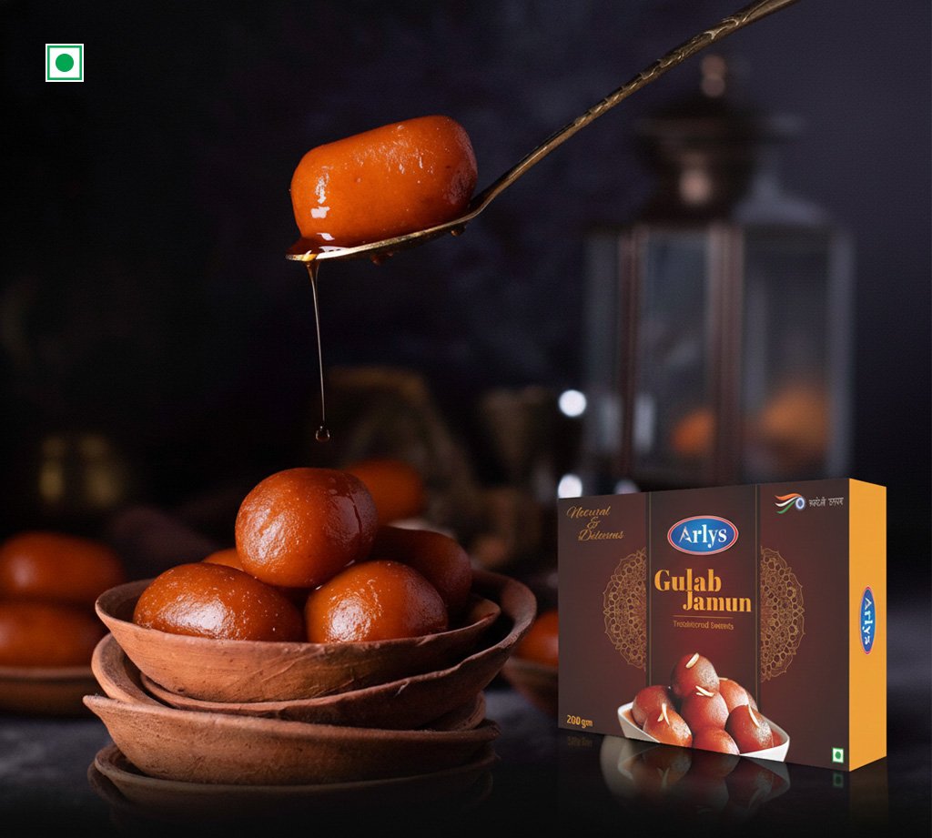 Syrup-dripping spoon hovering over a stack of gulab jamuns beside an Arlys Gulab Jamun box.