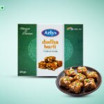 Arlys dodha burfi traditional sweets box with a plate of chopped burfi pieces topped with nuts on a mint backdrop