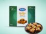 Arlys dodha burfi traditional sweets box with a plate of chopped burfi pieces topped with nuts on a mint backdrop