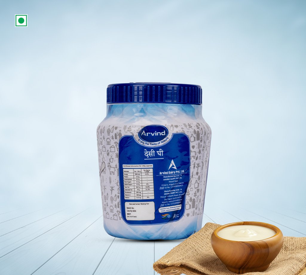 Blue-labeled Arvind dairy container with a dark blue cap sits on a pale wooden surface, next to a small wooden bowl of cream/yogurt.
