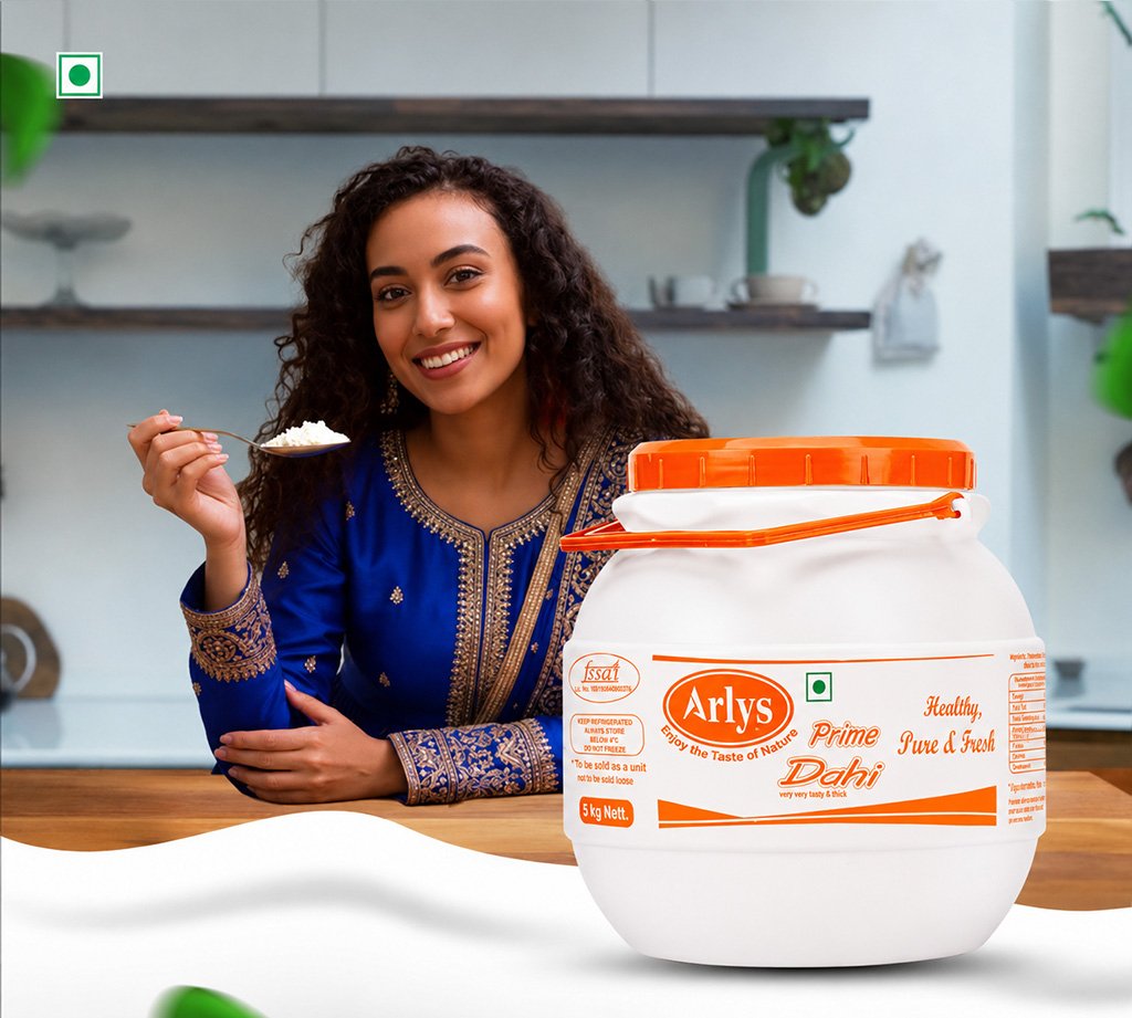 Smiling woman in a blue traditional kurta holding a spoonful of rice beside a large Arlys Dahi yogurt jar in a kitchen.