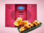 Pink Arlys Milk Cake box for traditional Sweets; plate of bite-sized fried cubes on a green tray in front.