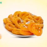 Plate of orange jalebi pastries arranged in a white bowl on a pale yellow background.